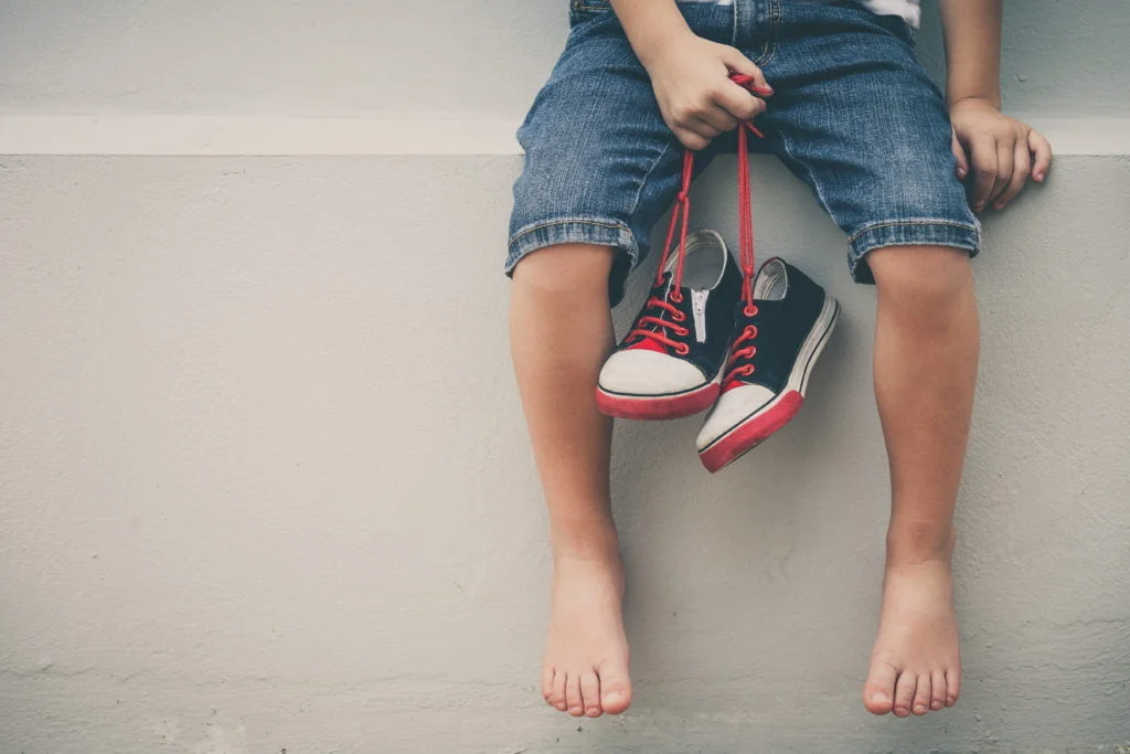 Little boy sitting near the house and keeping the youth sneaker Little boy sitting near the house and keeping the youth sneakers in his hands of at the day time.